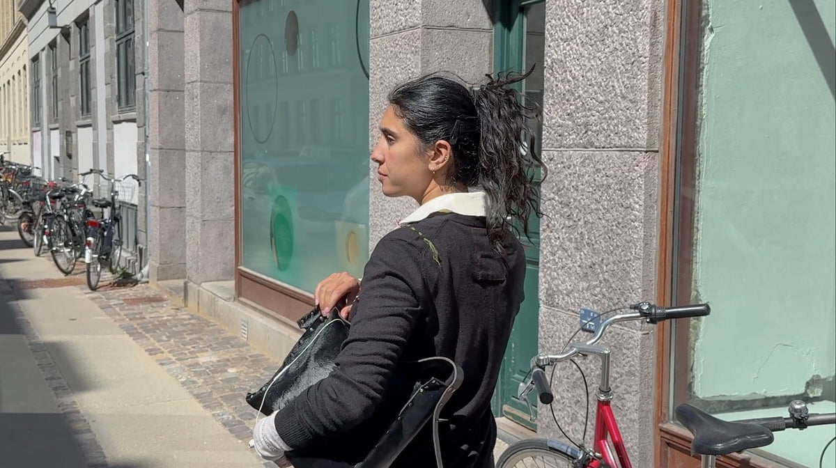 Side view of a model in an upcycled black knit cardigan with a leather bag in Copenhagen – RE;INCARNATED