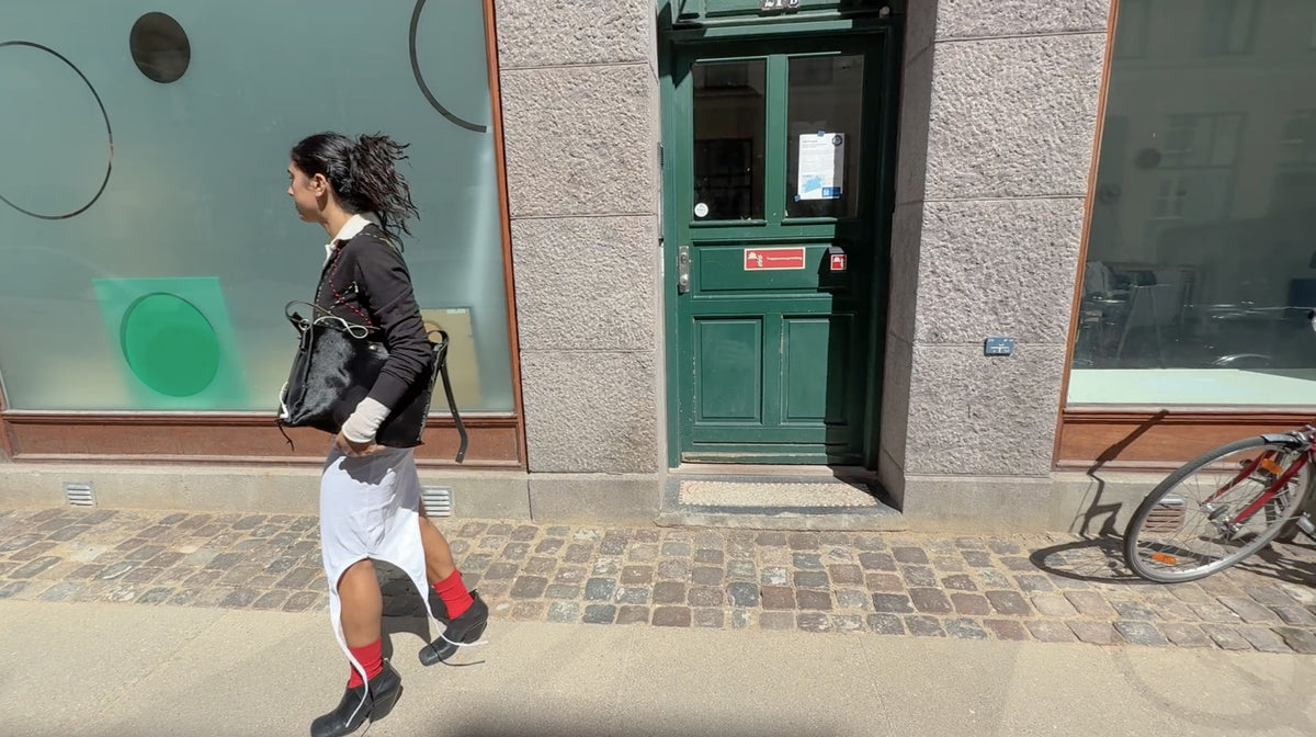Model walking in an upcycled black knit cardigan, white skirt and red socks in Copenhagen – RE;INCARNATED